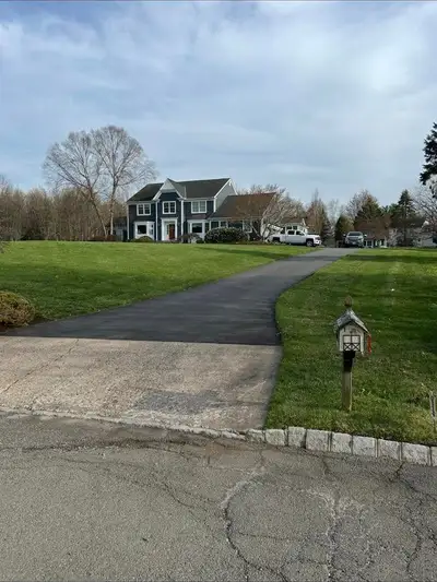 Wide shot of a large blue colonial with curved paved driveway, mowed lawn and mailbox.