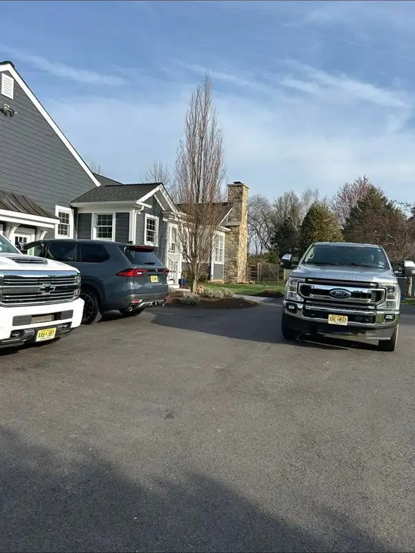 Three company work trucks and SUVs parked in a residential driveway beside a gray shingle house.