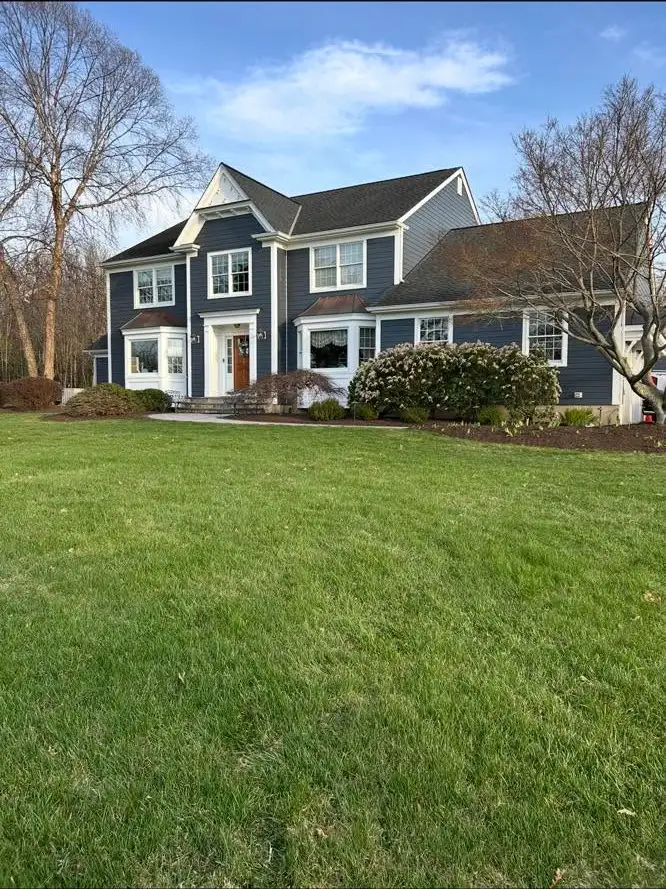 Front view of a two-story navy house with manicured lawn, foundation shrub beds and paved front walk.