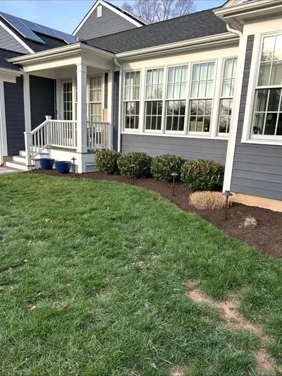 House exterior, mowed lawn, foundation mulch bed with shrubs and landscape light fixtures, solar panels on roof.