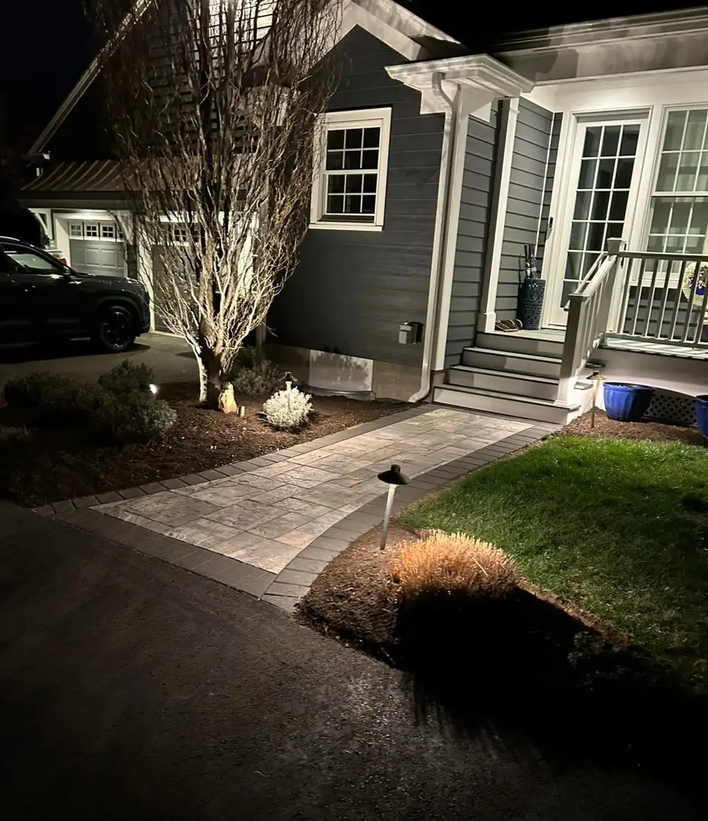 Night: paver front walkway with path lighting leading to porch steps, SUV and garage behind.