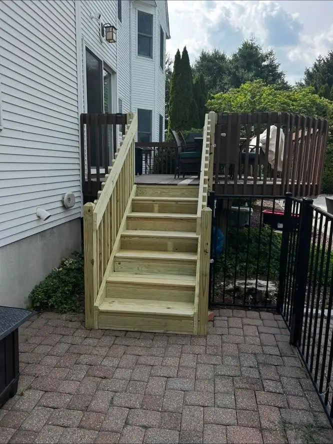 Brand new pressure-treated deck stairs leading down onto a paver patio.