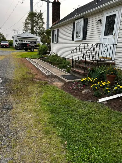 A new concrete walkway with a stone border, planted flower beds and iron-rail front steps.