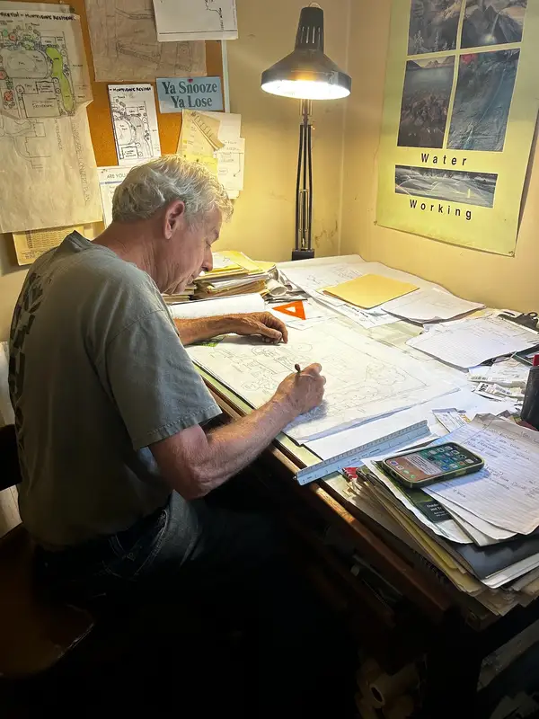 Jock draws a landscape plan by hand at his drafting table.