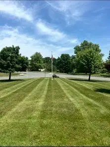 Freshly mowed striped lawn with flagpole, shade trees, and paved road behind.
