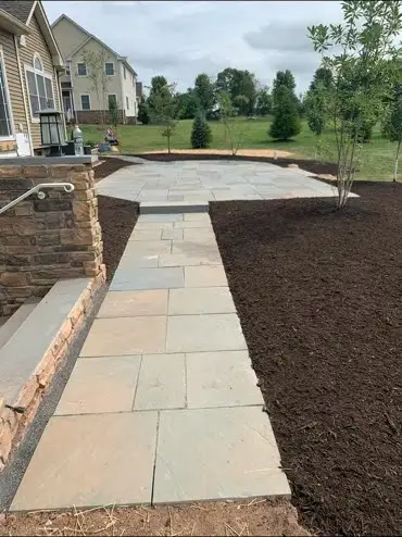 New flagstone walkway leading to flagstone patio, fresh dark mulch, stone wall and house left.